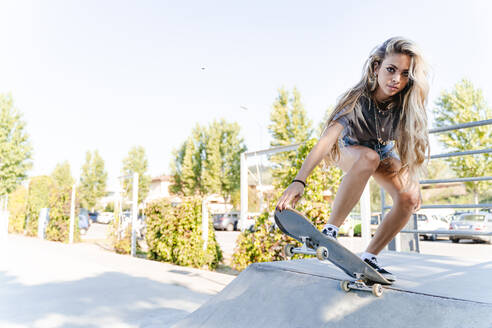 Selbstbewusste junge blonde Frau beim Skateboarden auf einer Rampe im Park - FMOF01170