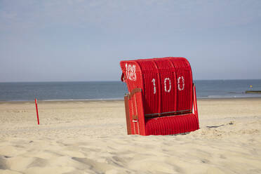 Red hooded chair on sandy beach against blue sky - WIF04321