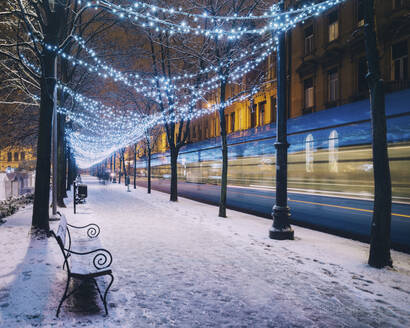 Unscharfe Bewegung einer Straßenbahn auf einem schneebedeckten Fußweg in einer beleuchteten Stadt zur Weihnachtszeit - LCUF00112