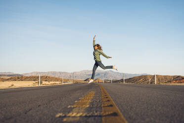 Carefree woman jumping on desert road against sky, Nevada, USA - DGOF01543