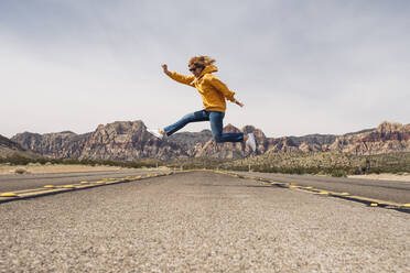 Unbekümmerte Frau springt auf Landstraße gegen Himmel, Nevada, USA - DGOF01545