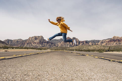 Carefree woman jumping on country road against sky, Nevada, USA - DGOF01545