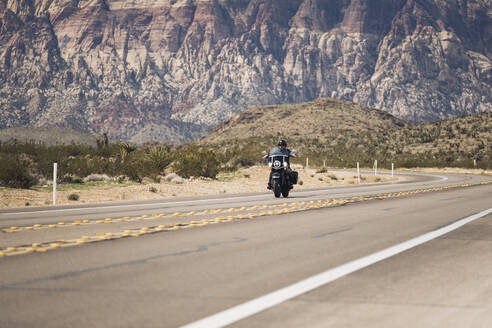 Mann fährt Motorrad auf dem Highway gegen einen Berg, Nevada, USA - DGOF01547