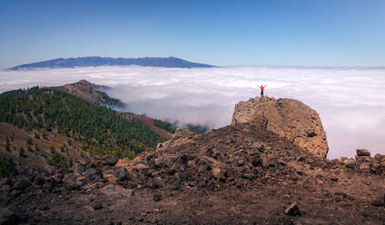 Rückenansicht eines anonymen männlichen Reisenden, der auf einem felsigen Hügel im Hochland steht und die herrliche Aussicht auf die Wolken genießt - ADSF15911