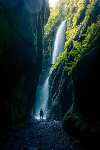 Back view of unrecognizable person walking of spectacular scenery of waterfall in long exposure in woods with green plants in highland area stock photo