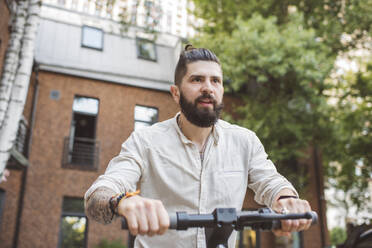 Hipster man riding electric push scooter in city - EYAF01334