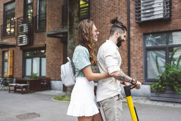 Glückliches Paar fährt elektrischen Roller auf der Straße in der Stadt - EYAF01335