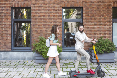 Happy couple with electric push scooter on footpath in city stock photo