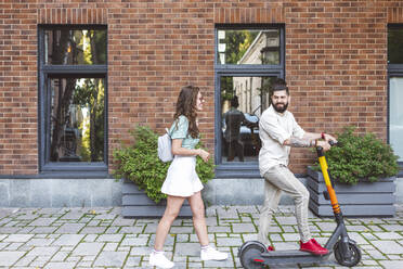 Glückliches Paar mit Elektro-Scooter auf dem Fußweg in der Stadt - EYAF01336