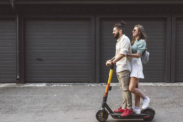 Smiling couple riding electric push scooter on street in city - EYAF01338