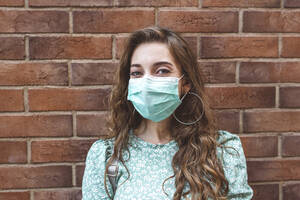 Woman wearing face mask against brick wall during COVID-19 outbreak - EYAF01342