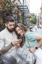 Hipster-Mann zeigt seiner Freundin das Smartphone, während er auf dem Gehweg steht - EYAF01348