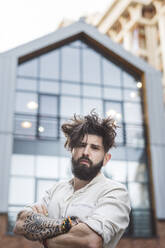 Hipster man standing with arms crossed against building in city - EYAF01352