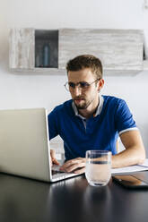 Handsome young man using laptop while doing homework at table - JRFF04733