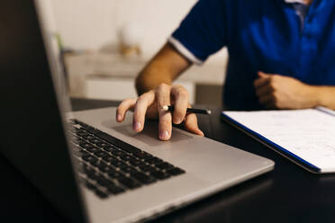Erwachsener männlicher Student, der einen Laptop benutzt, während er am Tisch Hausaufgaben macht - JRFF04745