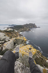 Tiefschnitt eines jungen männlichen Touristen über einer Felsformation vor bewölktem Himmel, Cíes-Inseln, Vigo, Provinz Pontevedra, Galicien, Spanien - RSGF00287