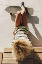 Blonde Afro-Frau mit Skateboard an einem sonnigen Tag liegend - MRRF00510