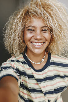 Happy Hispanic woman with blond curly hair taking selfie - MRRF00532