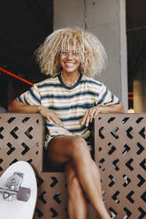 Fröhliche blonde Afro-Frau sitzt mit gekreuzten Beinen - MRRF00543