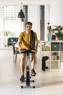 Young man cycling on exercise equipment at home - GIOF08940