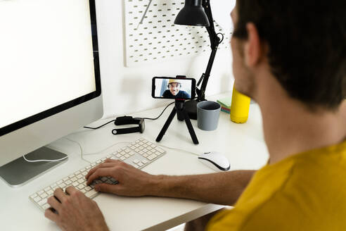 Young man talking on video call while working on computer at home - GIOF08968