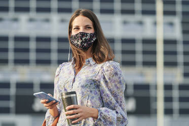Young woman wearing face mask using mobile phone while standing in city - KIJF03306
