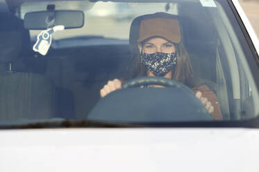 Junge Frau mit Gesichtsmaske beim Autofahren in der Stadt - KIJF03319