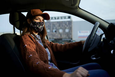 Young woman with cap and face mask driving car in city - KIJF03322