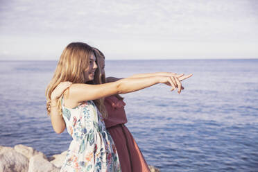 Friends pointing at sea with arms around on sunny day - DHEF00431