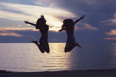 Friends jumping with arms outstretched against sea during sunset - DHEF00446