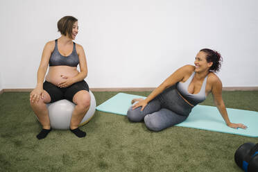 Pregnant woman sitting on fitness ball and exercise mat at yoga studio - MPPF01121