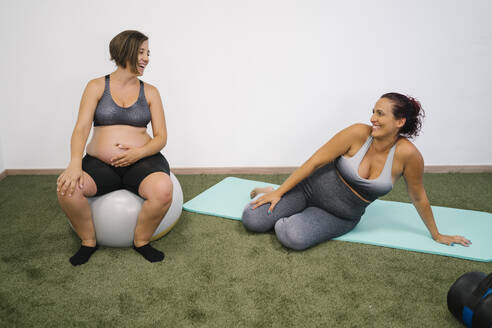 Schwangere Frau sitzt auf einem Fitnessball und einer Übungsmatte im Yogastudio - MPPF01121
