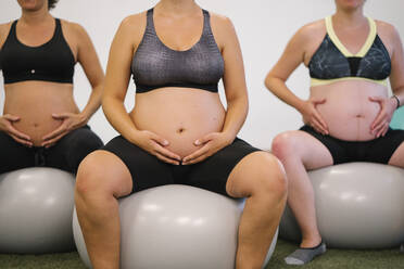 Midsection of pregnant woman sitting on fitness ball at yoga studio - MPPF01122