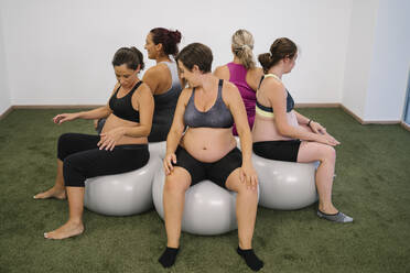 Schwangere Frau sitzt auf einem Fitness-Ball in einem runden Kreis im Yoga-Studio - MPPF01125