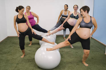 Pregnant woman with leg on fitness ball standing at yoga studio - MPPF01127