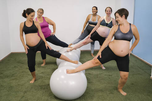 Schwangere Frau mit Bein auf Fitness-Ball stehend im Yoga-Studio - MPPF01127
