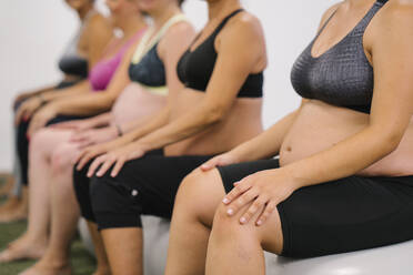 Mittelteil einer schwangeren Frau, die auf einem Fitnessball sitzt - MPPF01128