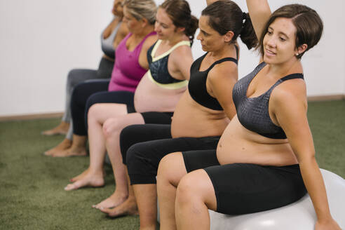 Schwangere Frau mit erhobener Hand auf Fitnessball sitzend - MPPF01130