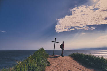 Wanderer am Gipfelkreuz stehend mit Blick auf das Meer gegen den Himmel bei Sonnenuntergang - KNTF05512