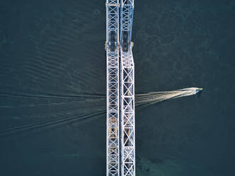 Aerial view of boat moving over Volga River under metallic railway bridge - KNTF05531