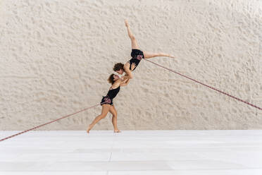 Aerial dancers dancing while hanging against wall - DLTSF01262