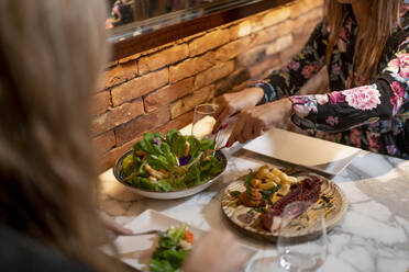 Friends eating garnish food while sitting on dinning table at restaurant - PGF00134