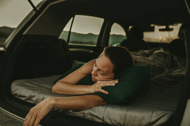 Müde Frau schläft im Kofferraum eines Autos in der Dämmerung - DMGF00147