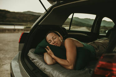 Müde Frau schläft in der Abenddämmerung im gemütlichen Kofferraum eines Autos - DMGF00148