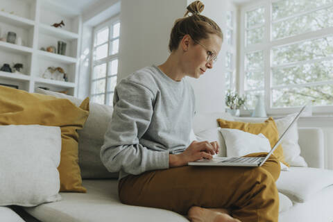 Mid adult woman working on laptop while sitting on sofa at home stock photo