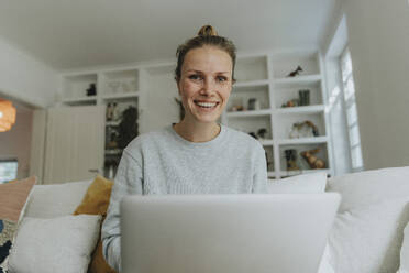 Woman smiling while working on laptop at home - MFF06200