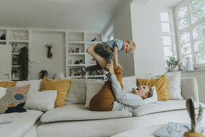 Mutter fasst ihren Sohn am Bein, während er zu Hause auf dem Sofa spielt - MFF06204