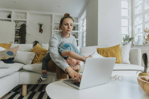 Die Mutter kümmert sich um den Jungen, während sie zu Hause am Laptop arbeitet - MFF06210