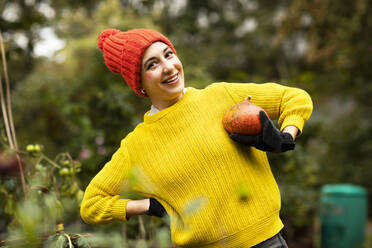 Smiling woman holding pumpkin while standing at urban garden - SGF02680