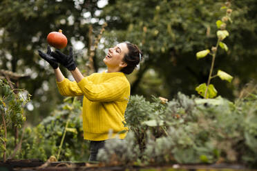 Woman playing with pumpkin while standing at urban garden - SGF02682